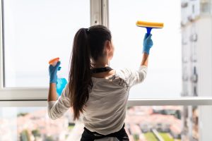 People, Housework And Housekeeping Concept. Happy Woman In Gloves Cleaning Window With Rag And Cleanser Spray At Home